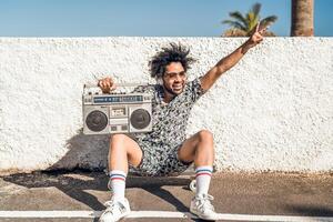 jung afro Latein Mann haben Spaß Hören Musik- mit Kopfhörer und Jahrgang Boombox während Sommer- Urlaube foto