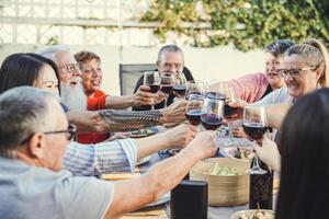 glücklich Familie Jubel mit rot Wein beim Wiedervereinigung Abendessen im Garten - - Senior haben Spaß Toasten Weingläser und Essen zusammen draussen - - Menschen und Essen Lebensstil Konzept foto