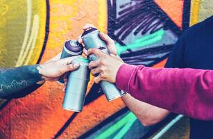 Gruppe von Graffiti Künstler Stapeln Hände während halten sprühen Farbe können gegen Wandgemälde Hintergrund - - jung Maler beim Arbeit - - Konzept von zeitgenössisch Kunst, Straße Kunst und Menschen Jugend Lebensstil foto