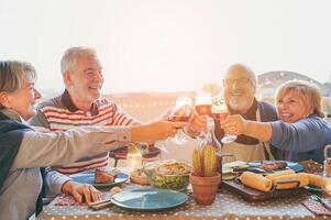 glücklich Senior freunde haben Spaß Jubel mit rot Wein beim Grill im Terrasse draussen - - reifen Menschen Herstellung Abendessen Toasten Brille und Lachen zusammen - - Freundschaft und Alten Lebensstil Konzept foto