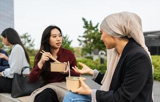 gemischtrassig Geschäft Frauen nehmen ein brechen zum Essen ein Mahlzeit draußen das Büro foto