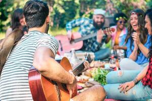 jung Menschen tun Picknick und spielen Gitarre im Park - - Gruppe von glücklich freunde haben Spaß während das Wochenende draussen - - Freundschaft, Essen und trinken, komisch Aktivitäten und Jugend Lebensstil Konzept foto