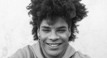 afro lächelnd Mann Porträt - - gemischt Rennen jung Kerl mit lockig Haar posieren im Vorderseite Kamera - - Jugend tausendjährig Generation Kultur und multi ethnisch Menschen Konzept - - schwarz und Weiß Bearbeitung foto