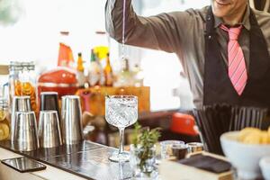 Barmann Mischen ein Cocktail im ein Kristall Glas im ein amerikanisch Bar - - Barmann Gießen Alkohol im ein Glas mit aromatisch Kräuter - - Beruf, Lebensstil, trinken Konzept foto