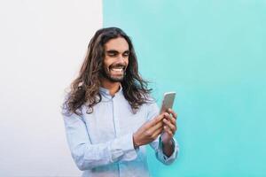 glücklich Mann mit Handy, Mobiltelefon Smartphone draussen - - Hipster Mode Kerl haben Spaß mit Sozial Medien Technologie Anwendungen - - Menschen Technik süchtig und Neu Medien Lebensstil Konzept - - Blau Hintergrund foto