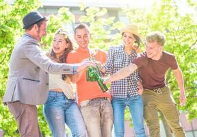 Gruppe von freunde genießen Biere draussen - - glücklich jung Menschen haben Spaß zusammen Toasten Flaschen von Bier im das Stadt - - Jugend Freundschaft Party Konzept - - Fokus auf links Mann Arm foto