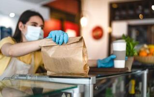 Bar Inhaber Arbeiten nur mit nehmen Weg Aufträge während Corona Virus Ausbruch - - jung Frau Arbeiter tragen Gesicht chirurgisch Maske geben Mitnahme Mahlzeit zu Kunden - - Gesundheitswesen und Essen trinken Konzept foto