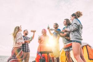 Gruppe von freunde haben Grill Trinken Biere während Camping auf das Strand - - glücklich Menschen genießen Lager Grill spielen Gitarre, Singen und Hören Musik- beim Sonnenuntergang - - Freundschaft, Abenteuer Konzept foto