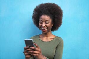 jung afro Frau mit Handy, Mobiltelefon Smartphone - - glücklich afrikanisch Mädchen haben Spaß mit Neu Trends Technologie Apps - - Jugend tausendjährig Generation z und Sozial Influencer Konzept - - Blau Hintergrund foto