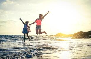 glücklich liebend Familie von Mutter und Tochter Springen im das Wasser beim Sonnenuntergang auf das Strand - - Mama mit ihr Kind haben Spaß zusammen auf ein Sommer- Tag - - Sommer, reisen, Ferien und Familie Konzept foto