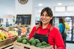 Latein Frau Arbeiten im Supermarkt halten ein Box enthält frisch Avocados foto
