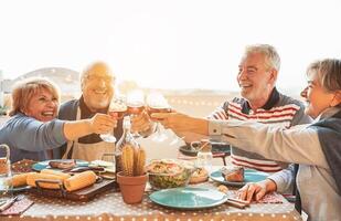 glücklich Senior Essen und Verkostung rot Wein Brille im Grill Abendessen Party - - Familie haben Spaß genießen Grill beim Sonnenuntergang Zeit auf Terrasse - - Alten Menschen Lebensstil und Essen und trinken Konzept foto