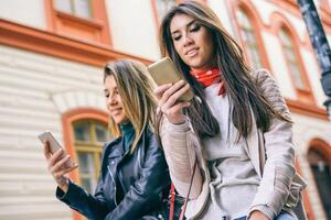 jung Frauen Stehen im ein städtisch Bereich mit Handy, Mobiltelefon Telefon im das Stadt - - glücklich freunde verbinden auf Sozial Medien Netzwerk draussen - - Menschen süchtig zu Neu Smartphone Technologie - - Fokus auf Hand auf richtig foto
