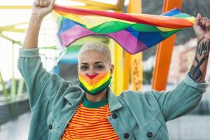 jung Frau tragen Fröhlich Stolz Maske halten Regenbogen Flagge Symbol von lgbtq Sozial Bewegung foto