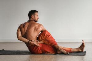 ein Mann mit ein nackt Torso tut Yoga drinnen. Fitness Trainer foto