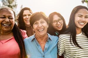 glücklich Mehrgenerationenhaus Frauen mit anders Alter und ethnische Zugehörigkeit haben Spaß lächelnd im Vorderseite von Kamera im ein Öffentlichkeit Park foto