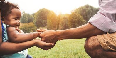 glücklich afrikanisch Familie haben Spaß zusammen im Öffentlichkeit Park - - schwarz Vater und Mutter halten Hand mit ihr Tochter - - afro Menschen und Elternteil Einheit Konzept foto