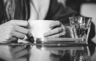 Frau Trinken ein warm Kaffee im ein Bar. weiblich Hände halten ein Tasse von heiß Getränk mit ein Glas Ö funkelnd Wasser. Getränke, Lebensstil, Menschen Konzept foto