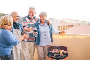 glücklich Senior freunde haben Spaß Trinken rot Wein beim Grill Abendessen im Terrasse - - reifen Menschen Essen und Lachen zusammen auf Dach - - Freundschaft und Alten Lebensstil Konzept foto