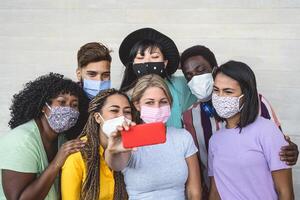 Gruppe jung Menschen tragen Gesicht Maske nehmen Selfie mit Handy, Mobiltelefon Smartphone draussen - - tausendjährig freunde mit anders Rennen und Kultur Porträt - - gemischtrassig und Technologie Konzept foto