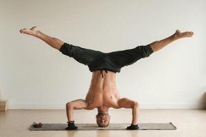 ein Mann mit ein nackt Torso tut Yoga Stehen auf seine Kopf drinnen. Fitness Trainer foto