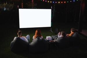 Familie Mutter, Vater und Kinder Uhr ein Beamer, Filme mit Popcorn im das Abend im das Hof foto