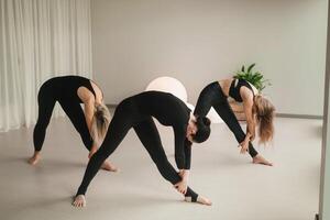 ein Gruppe von Mädchen im schwarz tun Yoga posiert drinnen. Frauen sind beschäftigt, verlobt im Fitness foto