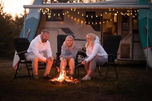 ein Familie Köche Würste auf ein Lagerfeuer in der Nähe von ihr Wohnmobil im das Wald foto