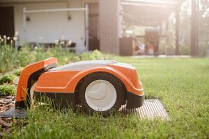 ein Orange Roboter Rasen Mäher steht auf das Base und ist berechnet von Elektrizität im das Hof foto