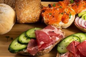 ein Sortiment von Sandwiches mit Fisch, Käse, Fleisch und Gemüse legen auf das Tafel und ein Brötchen foto