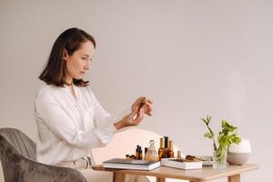das Aromatherapeut Mädchen ist Sitzung im ihr Büro und halten ein Flasche von aromatisch Öle. Dort sind wesentlich Öle auf das Tabelle foto