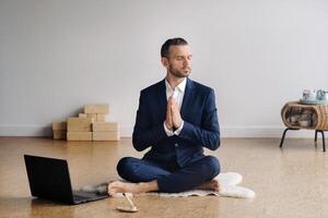 ein Mann im ein formal passen meditiert während Sitzung im ein Fitness Zimmer mit ein Laptop foto