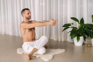 ein Mann mit ein nackt Torso tut Yoga im ein Fitness Zimmer. das Konzept von ein gesund Lebensstil foto