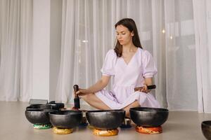 Porträt von ein weiblich Yoga Lehrer spielen ein tibetanisch Schüssel oder Singen ein Glocke im das Fitnessstudio während ein Yoga Rückzug foto