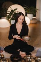 ein Frau im das Lotus Position mit ein Singen Schüssel drinnen . Entspannung und Meditation. Klang Therapie, Alternative Medizin. Buddhist Heilung Praktiken Methoden Ausübungen foto