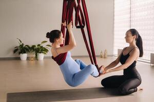 schwanger Mädchen. ein Frau mit ein Trainer tut Yoga im ein Hängematte im das Fitnessstudio. das Konzept von ein gesund Lebensstil, Mutterschaft foto