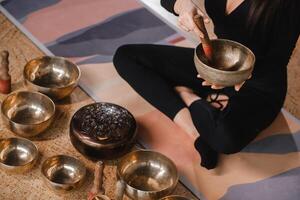 Nahansicht von ein Frau Hände Sitzung im ein Lotus Position mit ein Singen Schüssel drinnen. Entspannung und Meditation. Klang Therapie, Alternative Medizin. tibetanisch Schalen foto