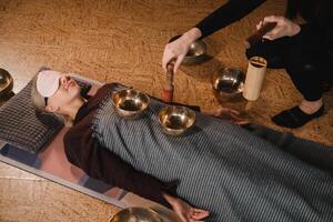 Nahansicht von das Hände von ein jung Frau Senden ein Botschaft mit das Hilfe von Singen Schalen und ein Koshi Glocke zu Ein weiterer Mädchen. Klang Therapie foto