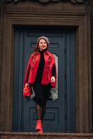 ein schön stilvoll Frau gekleidet im ein elegant rot Mantel mit ein stilvoll rot Handtasche im das Herbst Stadt foto