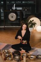 ein Frau im das Lotus Position mit ein Singen Schüssel drinnen . Entspannung und Meditation. Klang Therapie, Alternative Medizin. Buddhist Heilung Praktiken Methoden Ausübungen foto