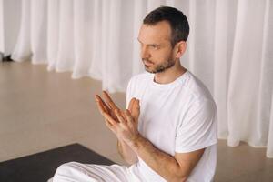 ein Mann im Weiß Sportbekleidung ist tun Yoga mit ein Fitness Zimmer. das Konzept von ein gesund Lebensstil foto