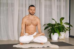 ein Mann mit ein nackt Torso tut Yoga im ein Fitness Zimmer. das Konzept von ein gesund Lebensstil foto