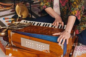 Hände von ein Frau Sitzung auf das Fußboden und spielen das Harmonium während das trainieren von Kundalini Yoga foto