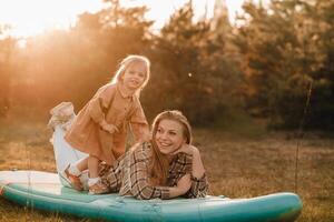 Mama und Tochter auf ein sup Tafel im das Wald beim Sonnenuntergang foto