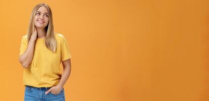 ziemlich und zärtlich süß europäisch weiblich unabhängig Freiberufler im Gelb T-Shirt Seufzen berühren Hals und Blick verträumt beim Oberer, höher richtig Ecke mit angenehm lächeln, posieren Über Orange Hintergrund foto