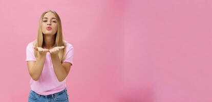 feminin und flirty charmant ziemlich Mädchen mit Braun gebrannt Haut und Messe Gerade Haar halten Palmen in der Nähe von gefaltet Lippen Senden Luft Kuss beim Kamera mit sinnlich Ausdruck posieren Über Rosa Hintergrund foto