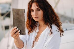 sexy Frau im ein Weiß Hemd sieht aus im das Spiegel auf ihr Privat Weiß Yacht foto