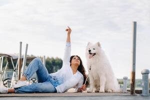 ein glücklich Frau mit ein groß Weiß Hund Lügen auf ein Seebrücke in der Nähe von das Meer beim Sonnenuntergang foto