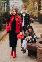 ein stilvoll Familie von drei Spaziergänge durch das Herbst Stadt posieren zum ein Fotograf . Papa, Mama und Tochter im das Herbst Stadt foto