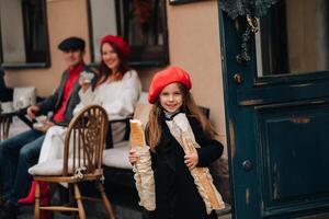 ein stilvoll Mädchen mit Baguettes steht in der Nähe von das Geschäft gegen das Hintergrund von ihr Eltern foto